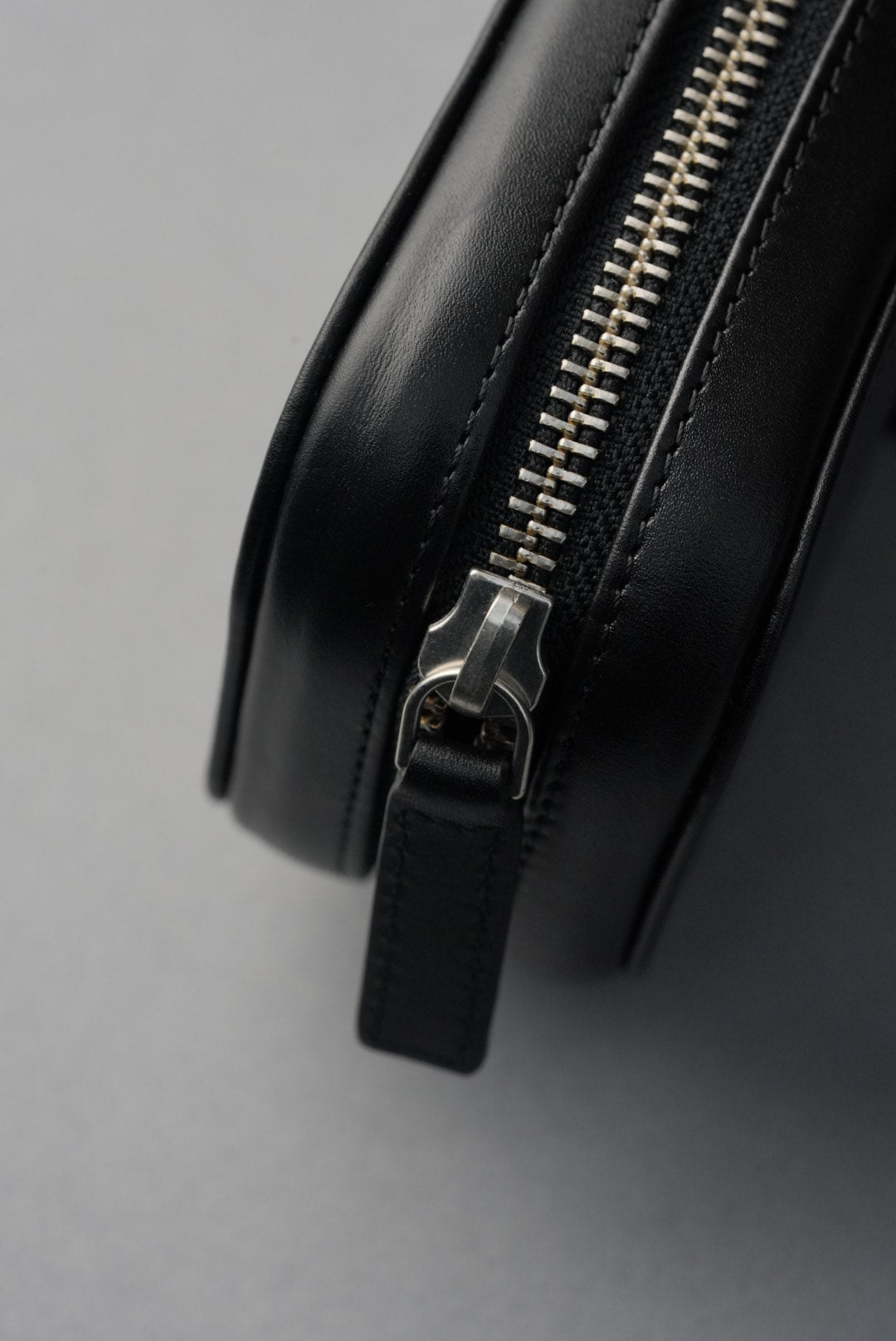 Close-up of a black leather bag with a silver zipper on a gray background