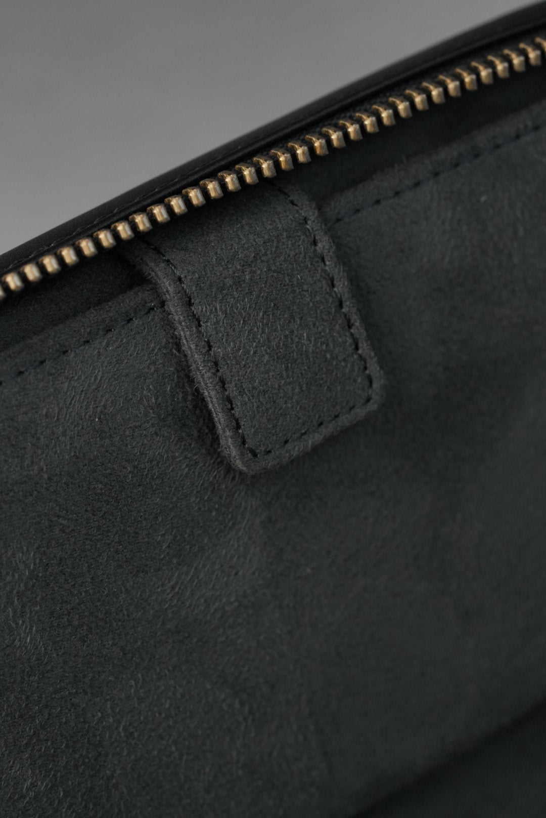 Close-up of a black leather jacket with a zipper detail on a gray background