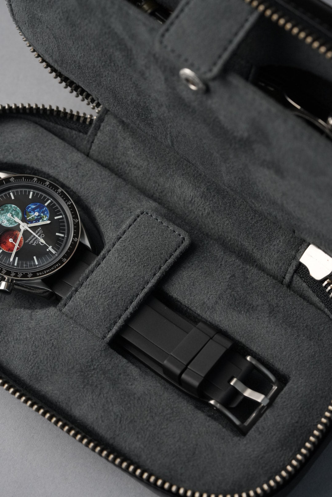 Black leather wallet with a watch on top against a gray background