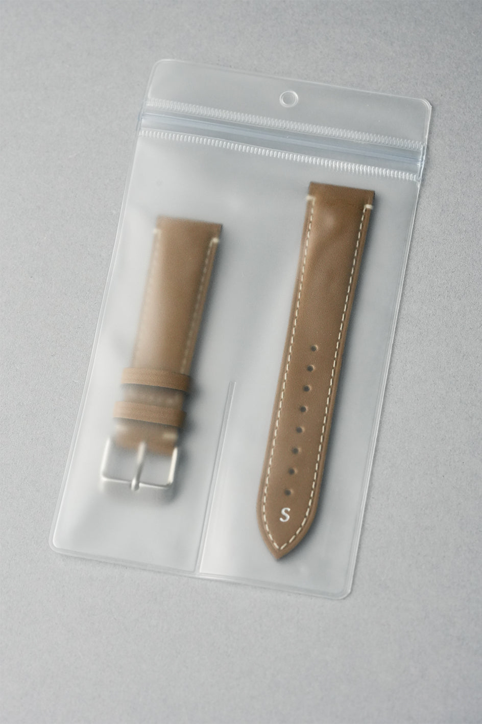 Two brown watch straps in clear packaging on a gray background