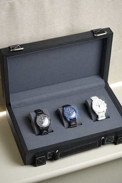 Black watch display case with three watches on a light gray background