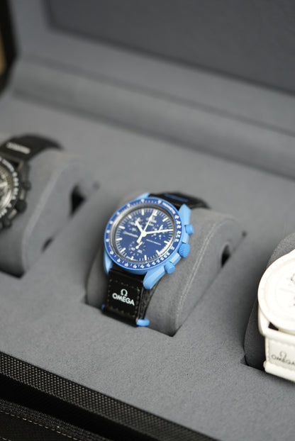 Close-up of a watch with a blue face and black strap on a gray surface.
