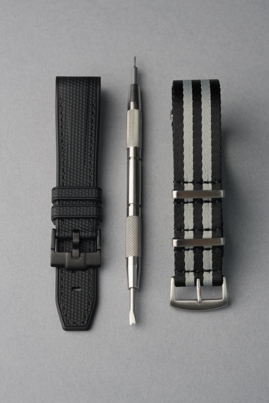 Two watch straps and a tool on a gray background