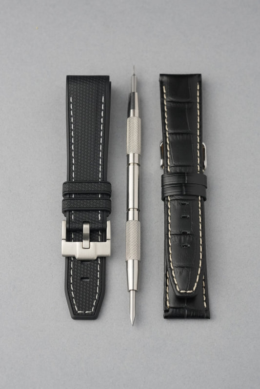 Two black watch straps with silver buckles and a small tool on a gray background