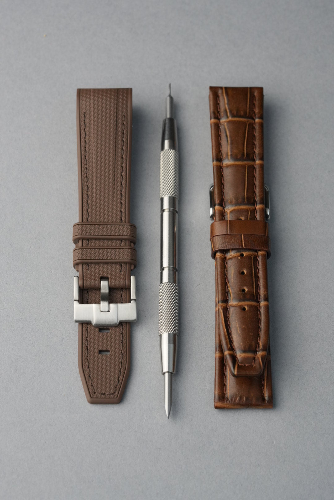 Two brown watch straps with silver buckles on a gray background
