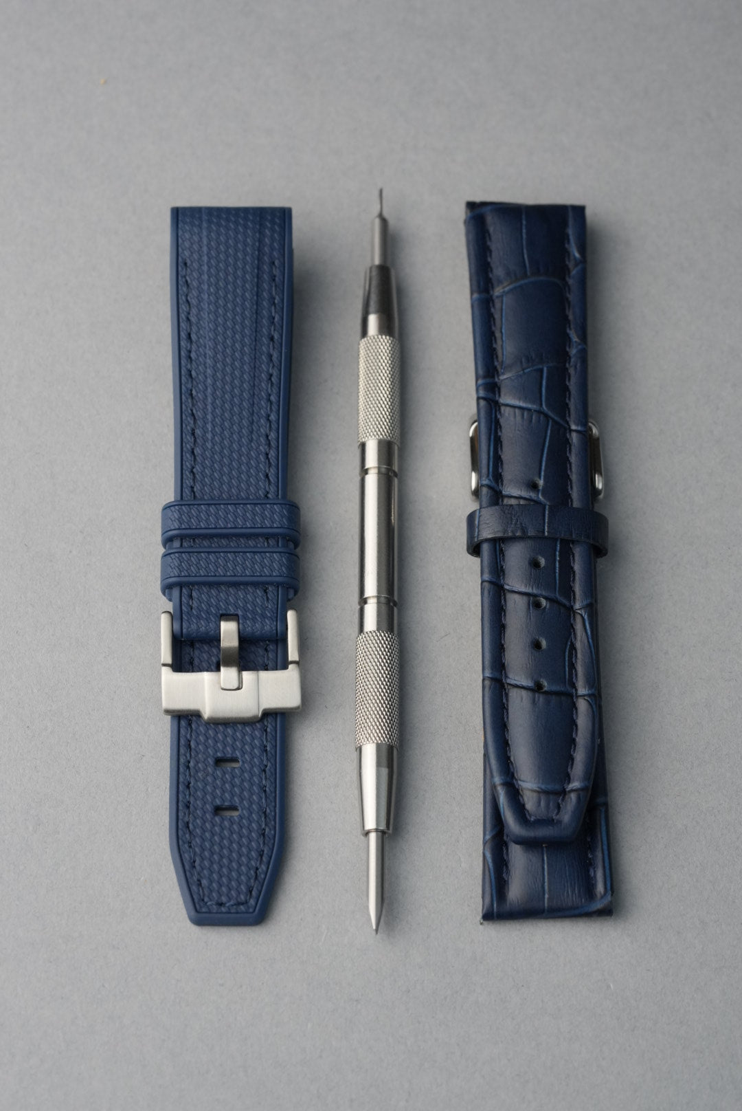Two blue watch straps and a tool on a gray background