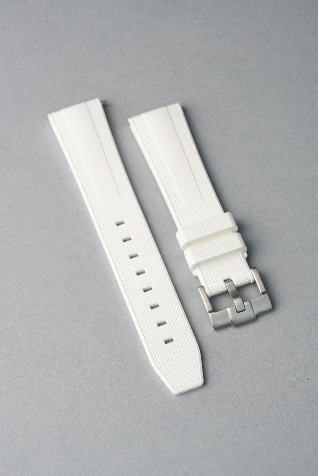 White watch strap with silver buckle on a gray background