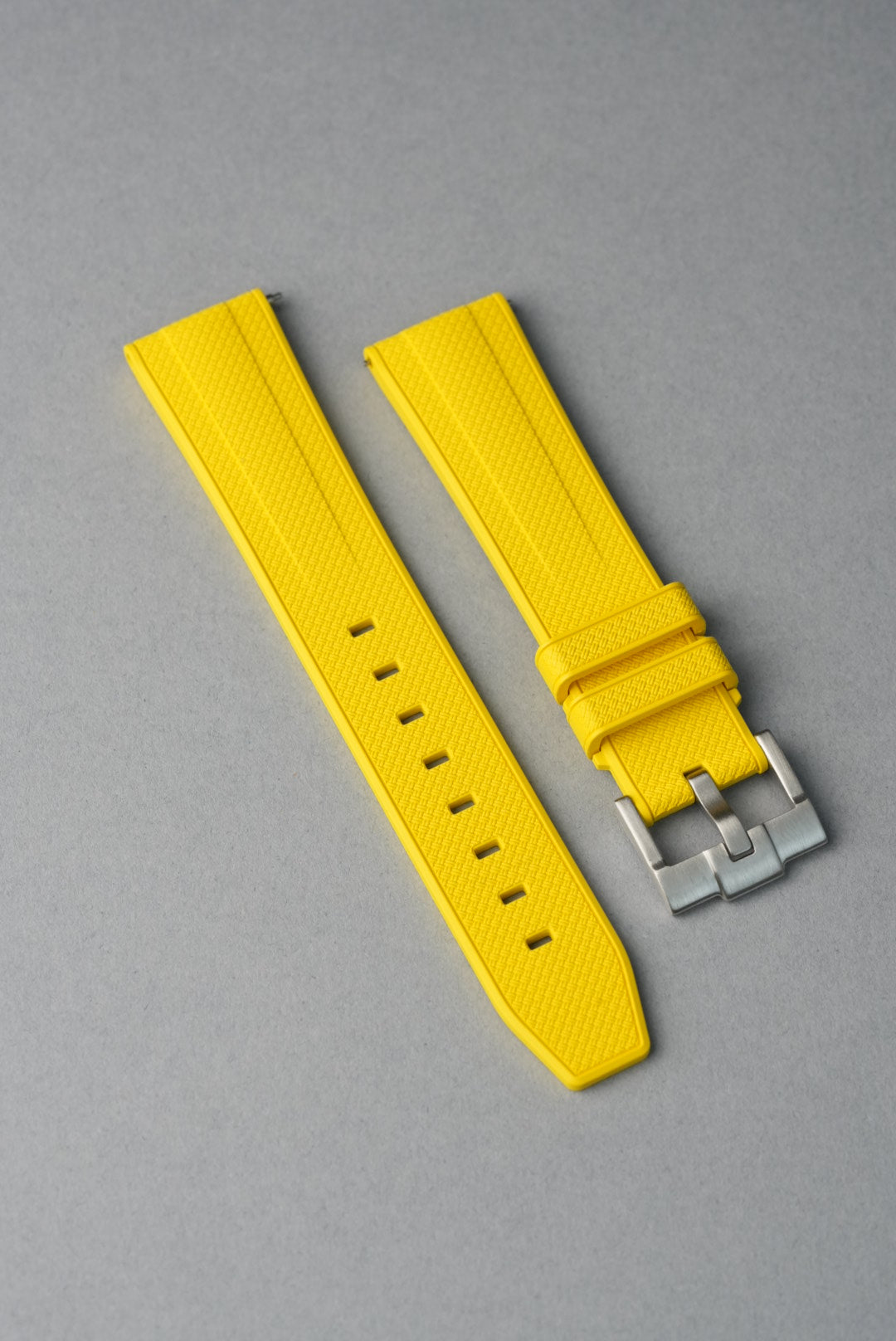 Yellow watch strap with silver buckle on a gray background