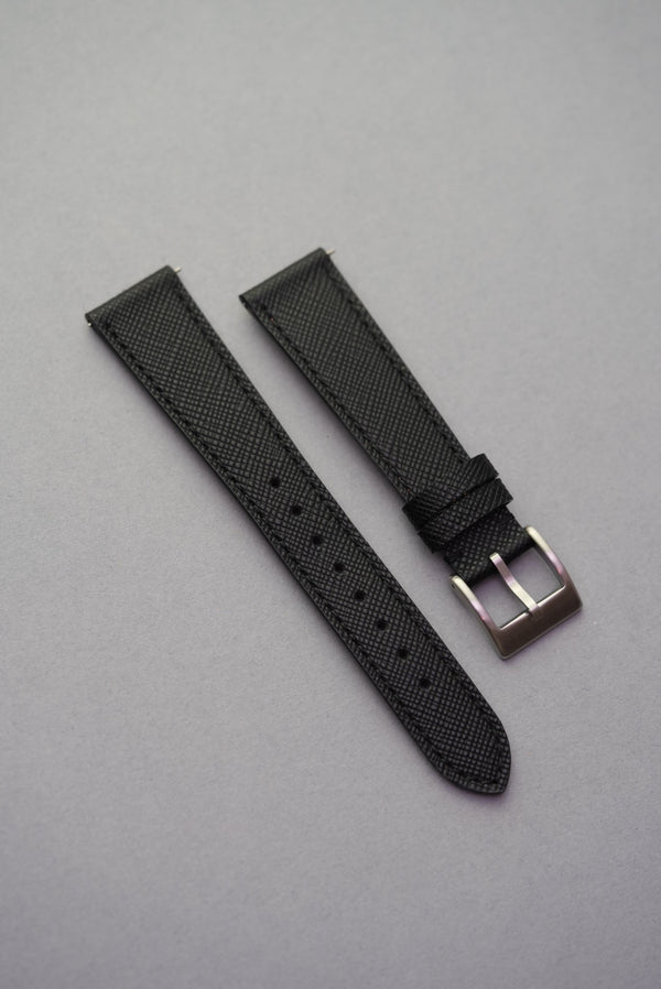 MoonSwatch black Saffiano leather strap with polished steel buckle — flat lay on grey background