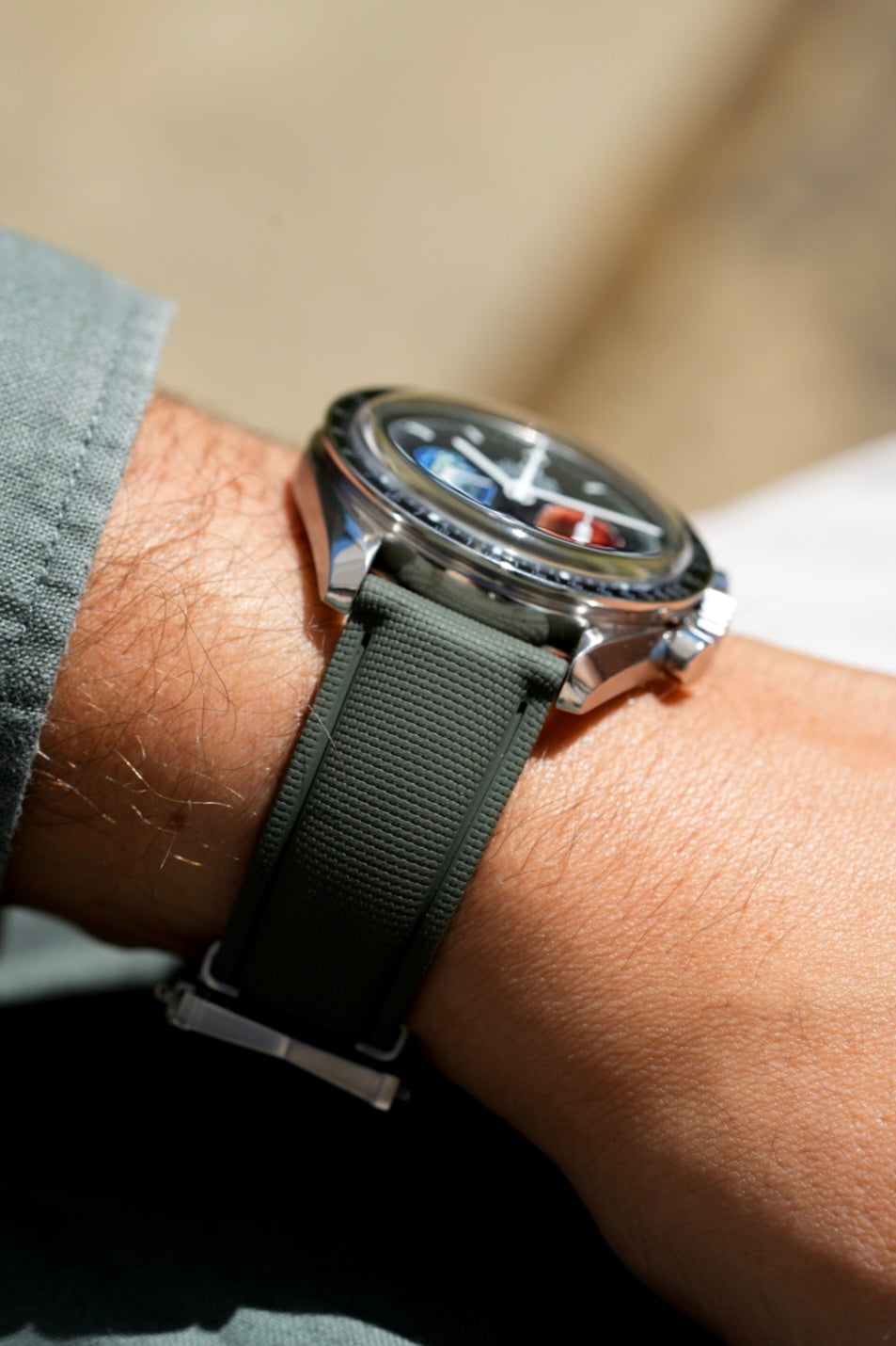 Watch with a gray strap on a wrist against a neutral background