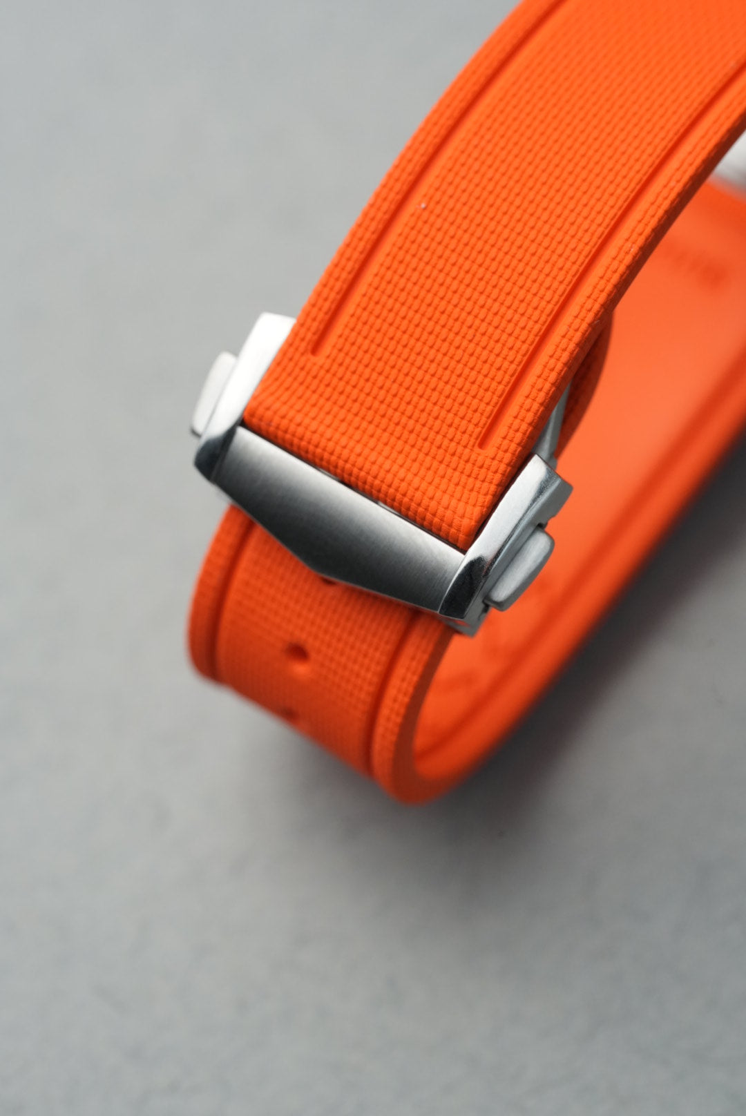 Close-up of an orange strap with a silver buckle on a gray background