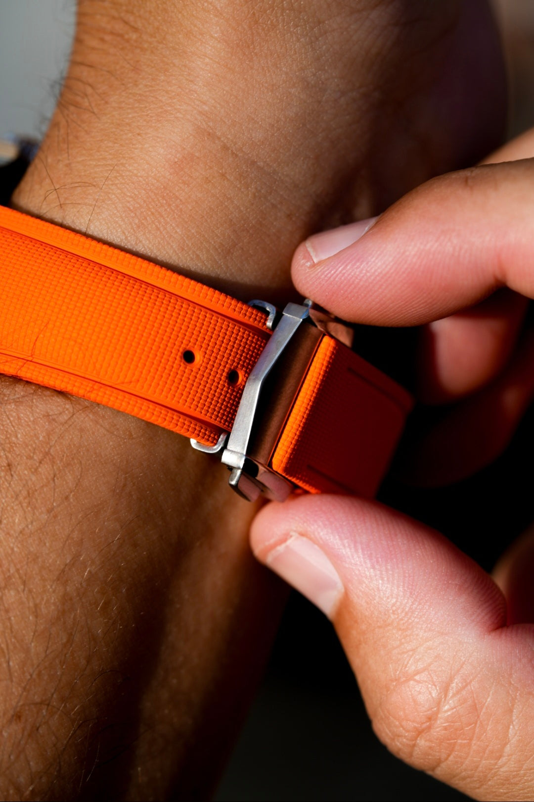 Person adjusting an orange belt with a metal buckle.