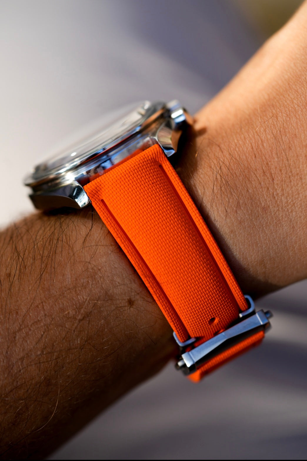 Watch with an orange strap on a wrist against a blurred background