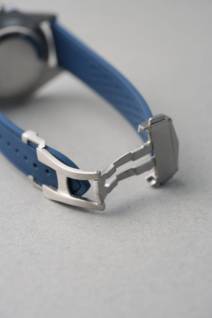 Close-up of a blue watch strap with a silver clasp on a gray background