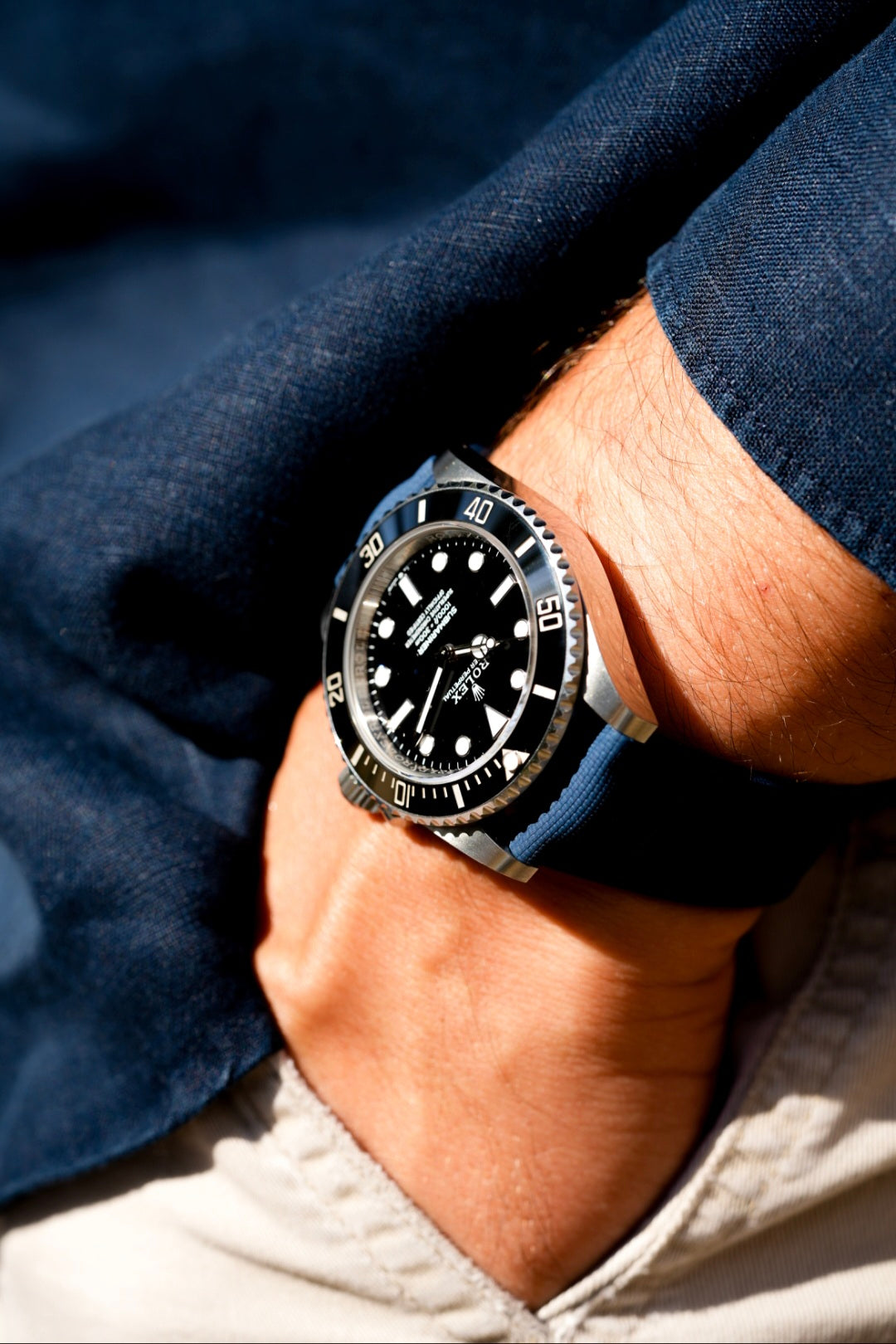 Close-up of a person wearing a watch with a dark face and silver case on a blue shirt.