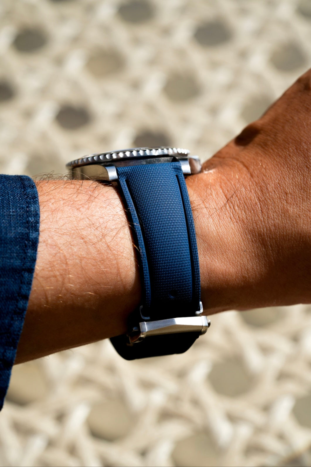 Close-up of a wrist wearing a watch with a blue strap against a blurred background