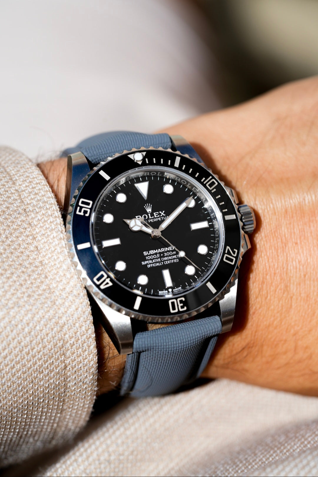 Rolex watch with blue strap on a wrist against a neutral background