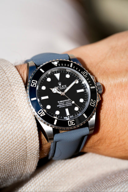 Rolex watch with blue strap on a wrist against a neutral background