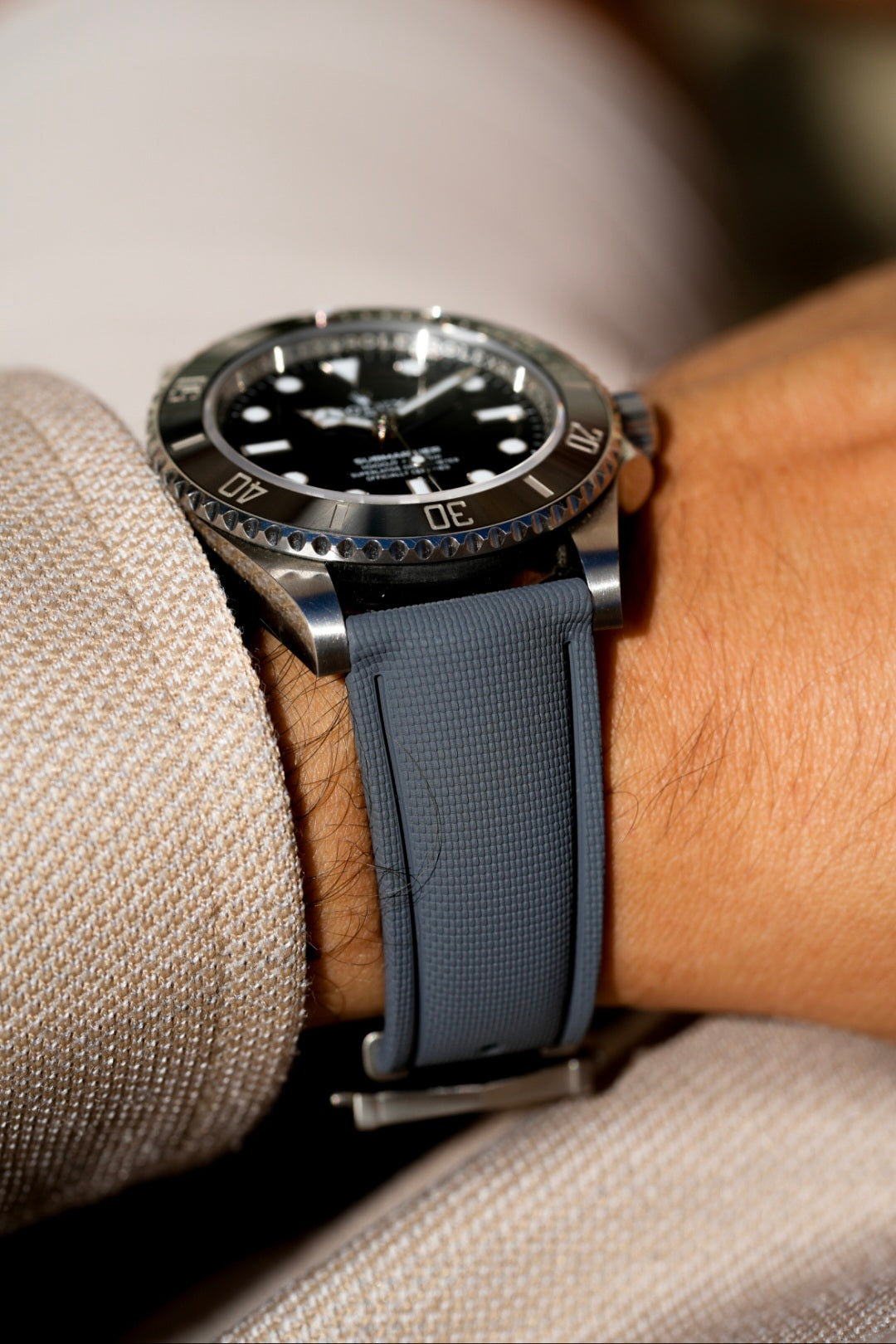 Watch with a dark strap on a wrist against a neutral background
