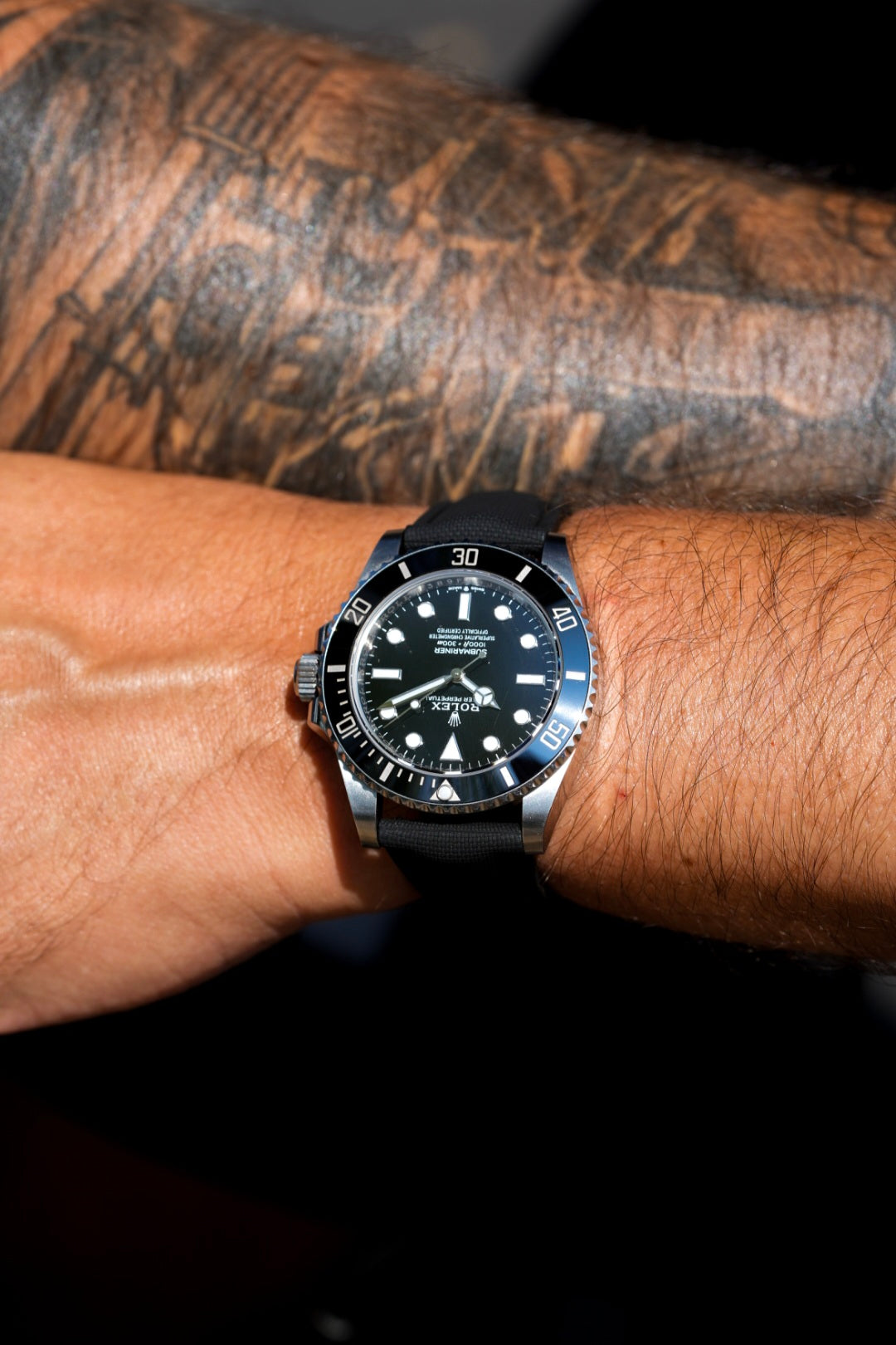 Black wristwatch on a tattooed arm with a dark background