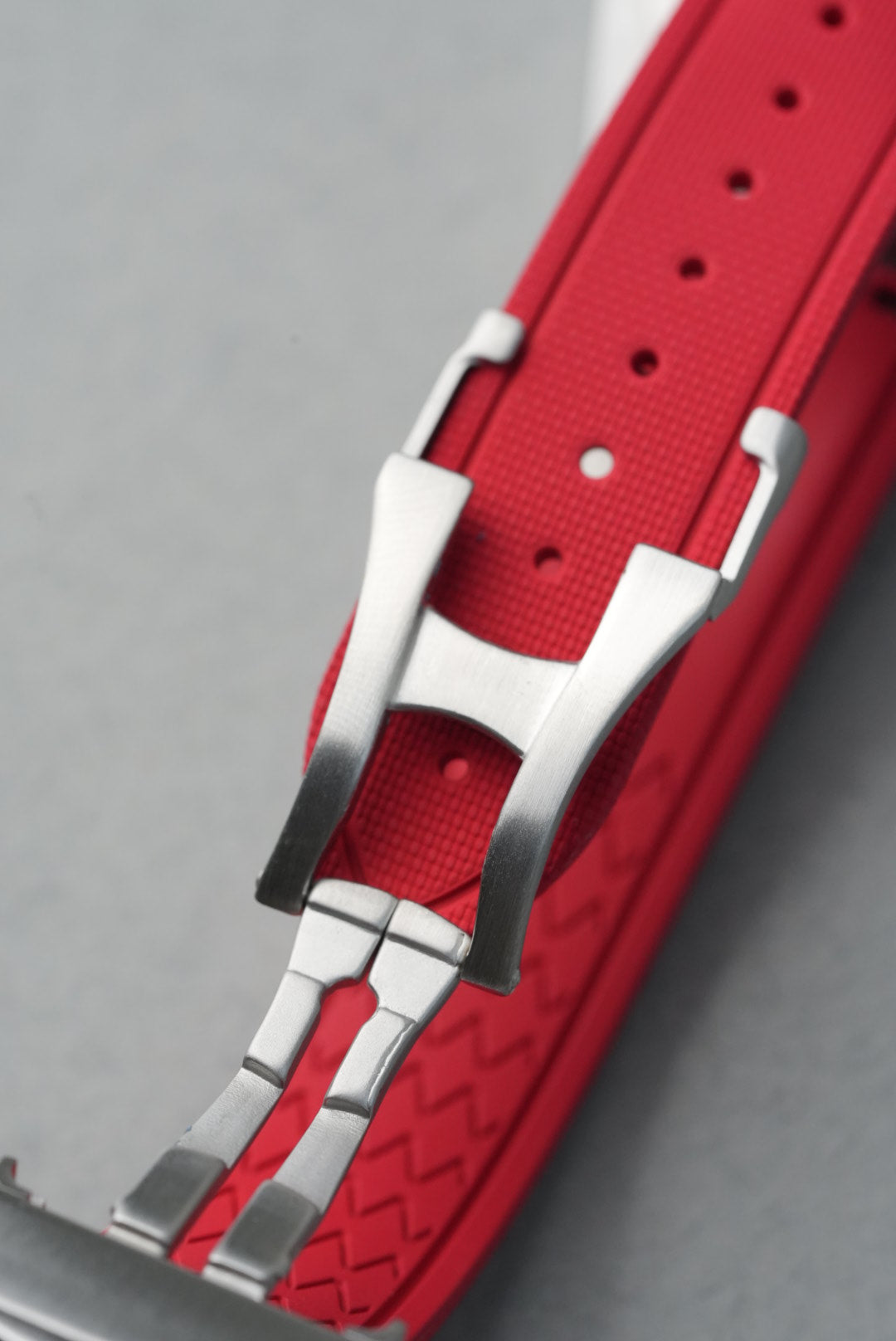Red watch strap with silver clasp on a gray background