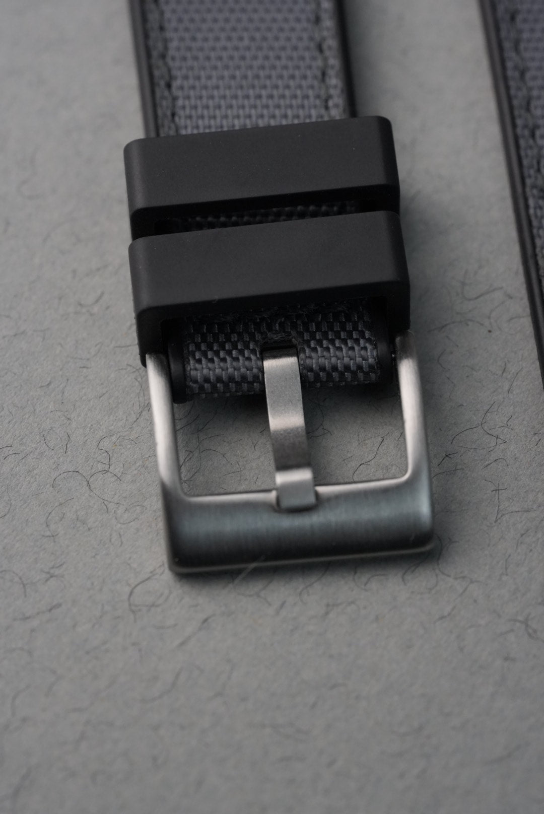 Close-up of a black belt with a silver buckle on a gray textured background