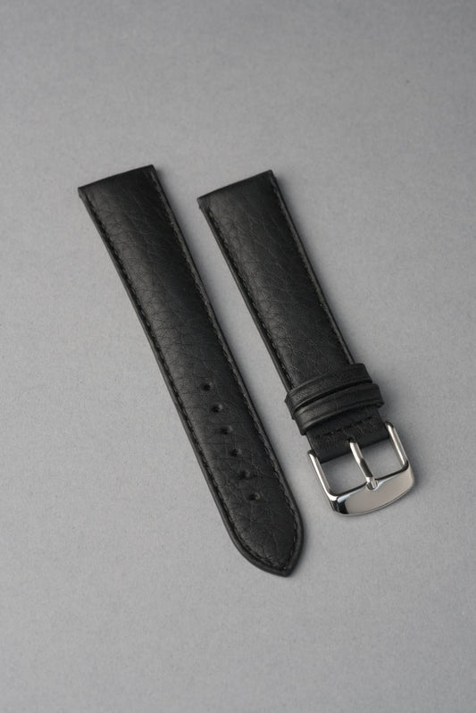 Black leather watch strap with silver buckle on a gray background