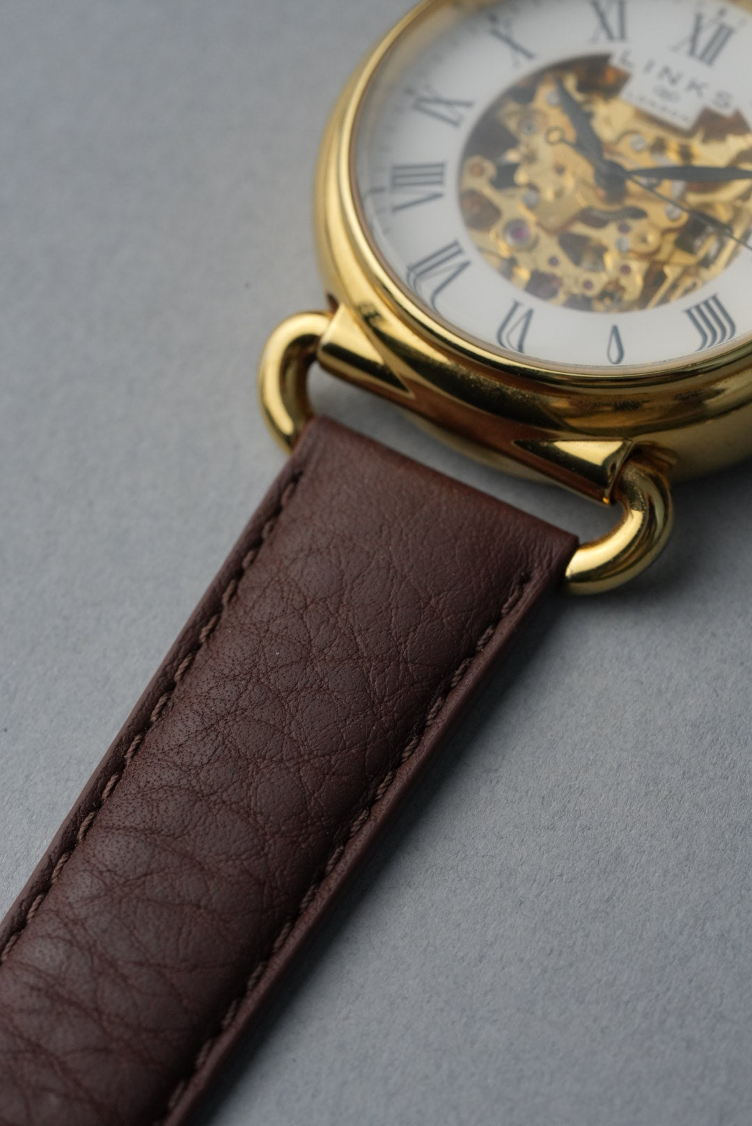 Watch with brown leather strap and gold casing on a gray background
