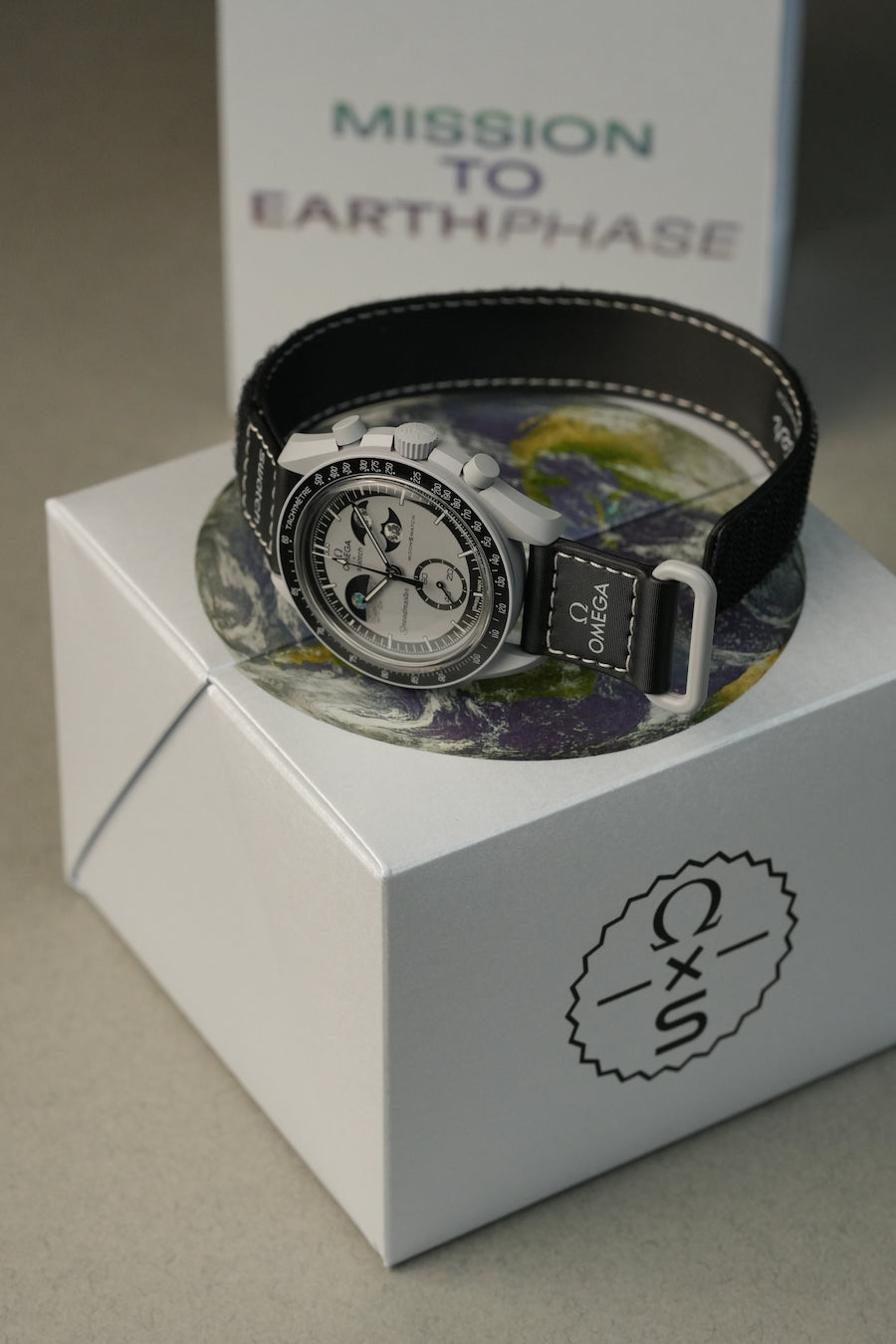 Watch with a black strap on a white box labeled 'Mission to Earthphase'.