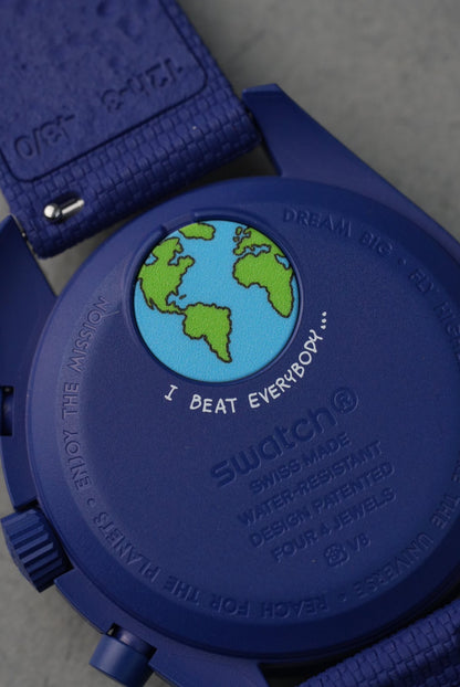 Close-up of a blue Swatch watch with a world map design on the back.