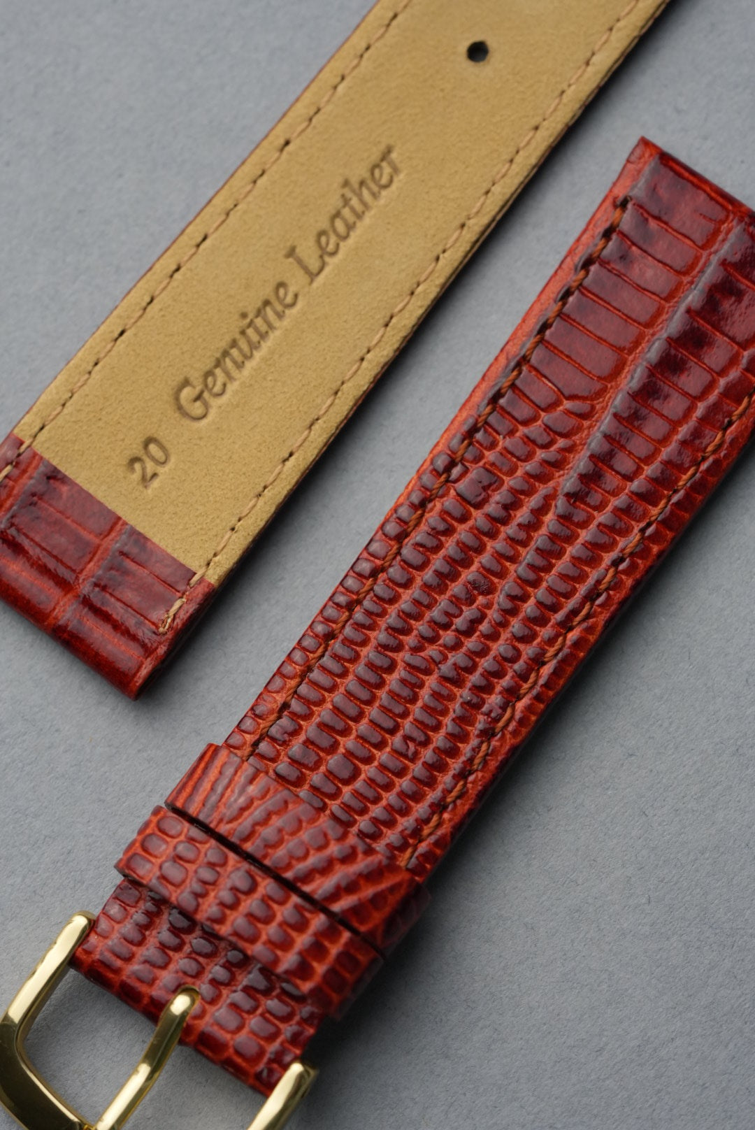 Red lizard skin watch strap with gold buckle on a gray background, featuring 'Genuine Leather' label.