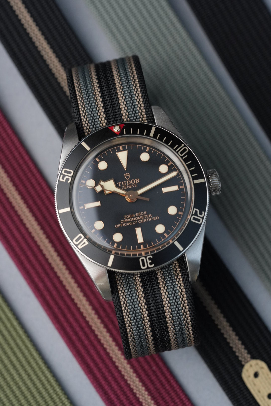 Tudor watch with a black face and striped strap on a striped background
