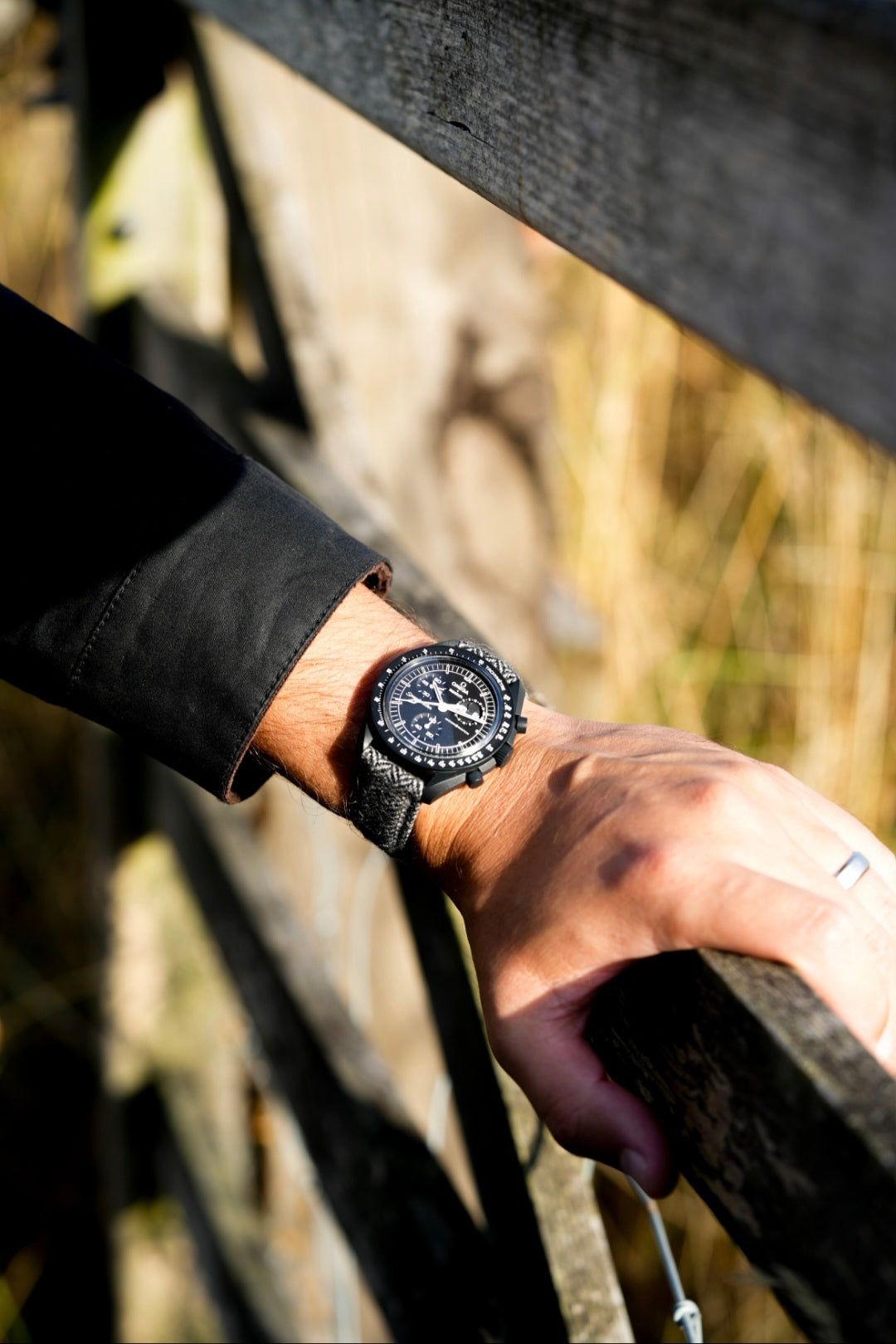 Hand wearing a black watch on a wooden fence with blurred natural background