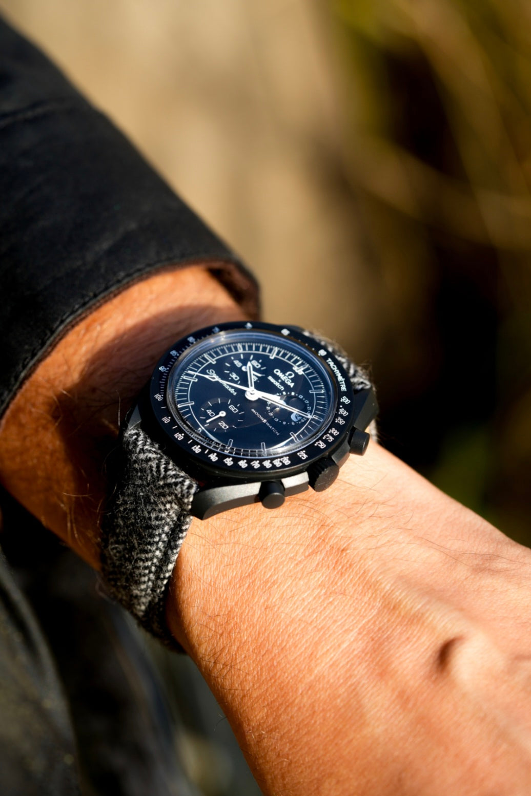 Person wearing a watch with a detailed face on a blurred natural background