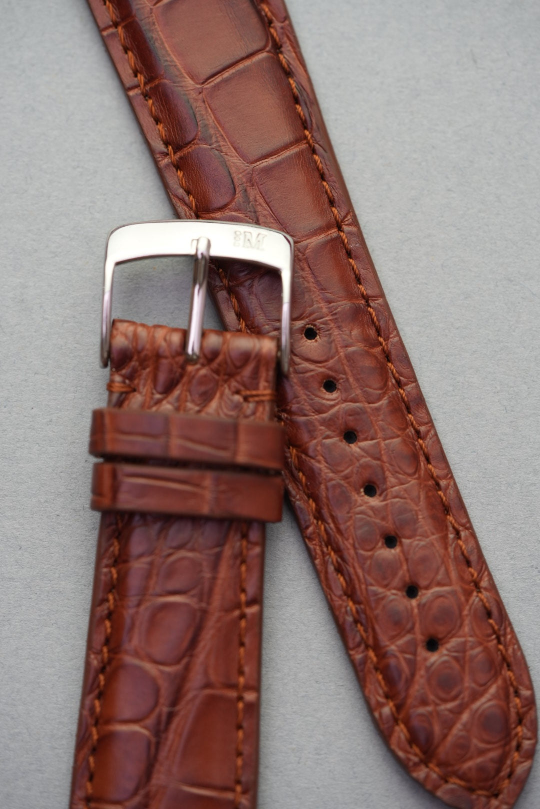 Polished buckle and embossed alligator pattern on brown leather strap