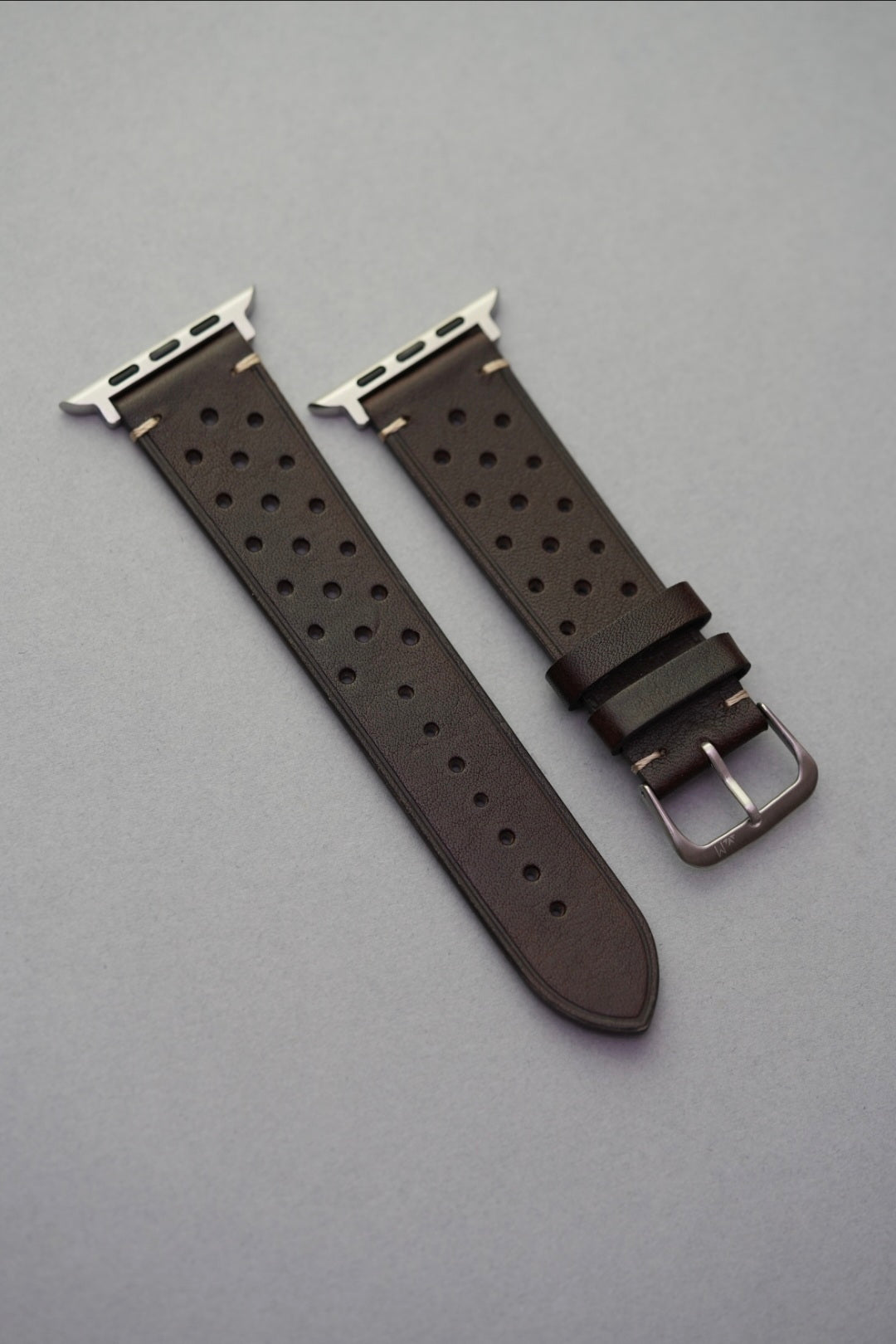 Perforated dark brown leather strap with Apple Watch adapters – flat lay view