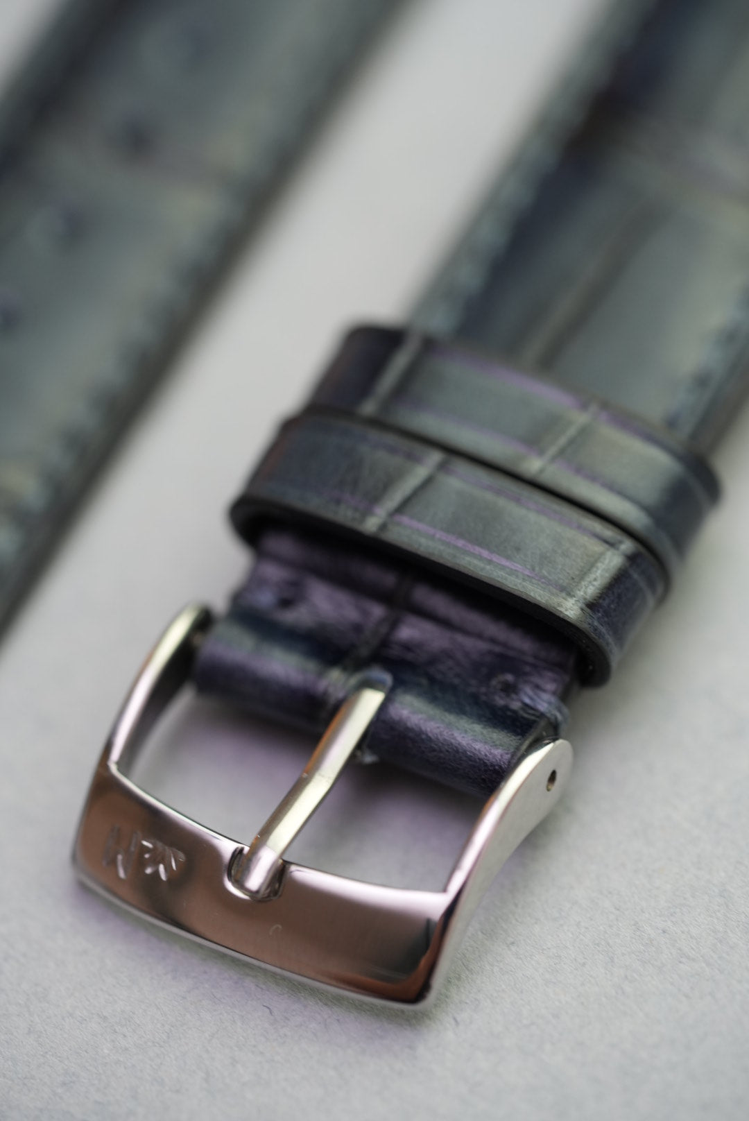 Close-up of buckle engraving on black calfskin alligator grain strap for Apple Watch.