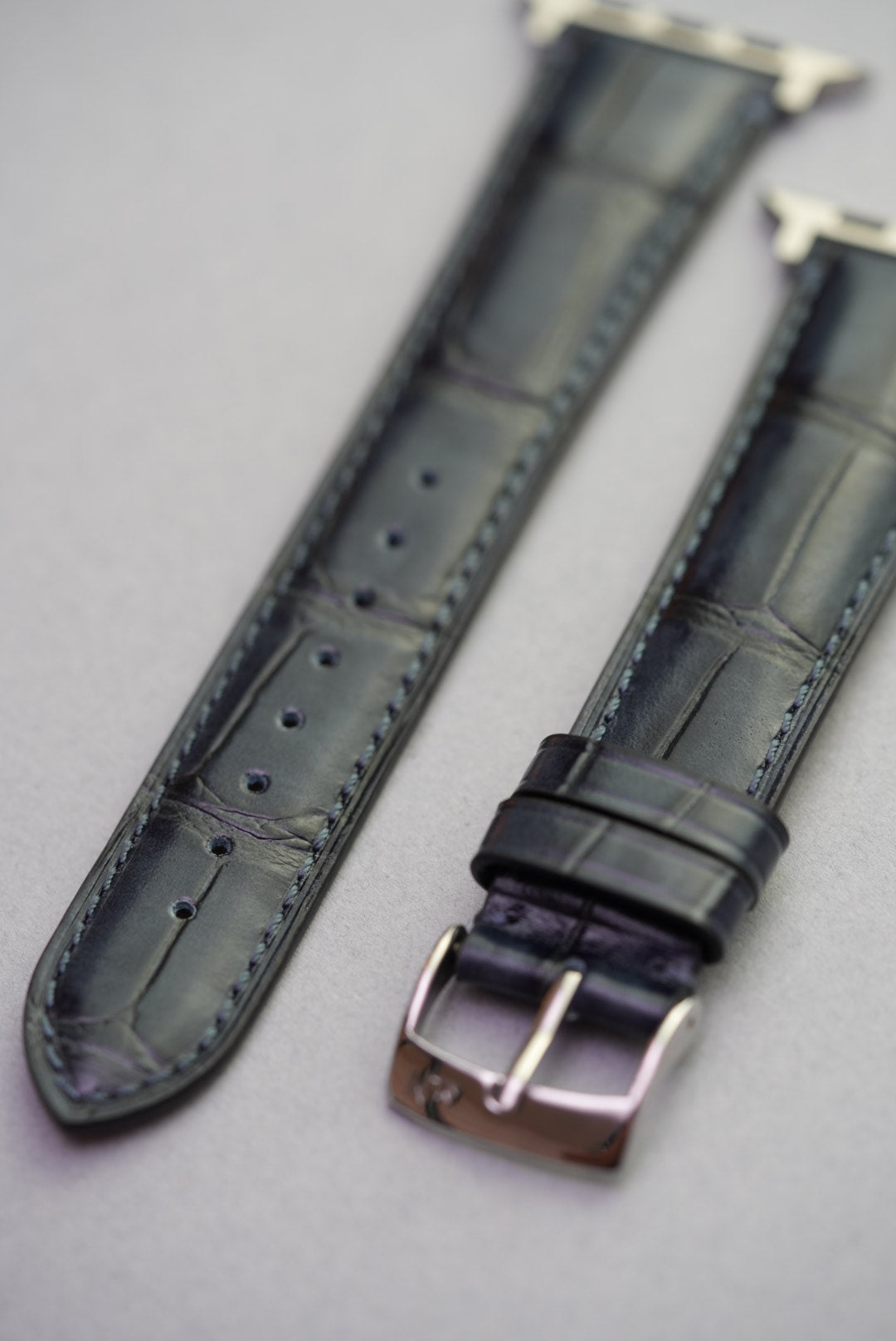 Close-up of black alligator grain calfskin leather watch strap for Apple Watch with polished buckle.Close-up of black alligator grain calfskin leather watch strap for Apple Watch with polished buckle.