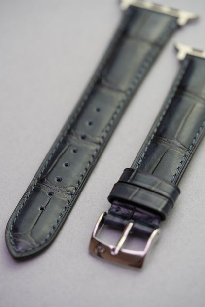 Close-up of black alligator grain calfskin leather watch strap for Apple Watch with polished buckle.Close-up of black alligator grain calfskin leather watch strap for Apple Watch with polished buckle.