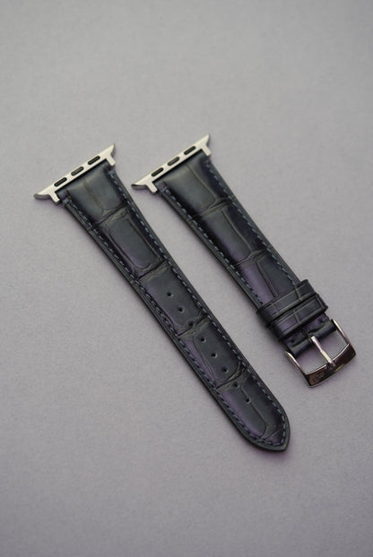 Top-down view of black embossed alligator leather strap for Apple Watch, showcasing detailed grain and stitching.