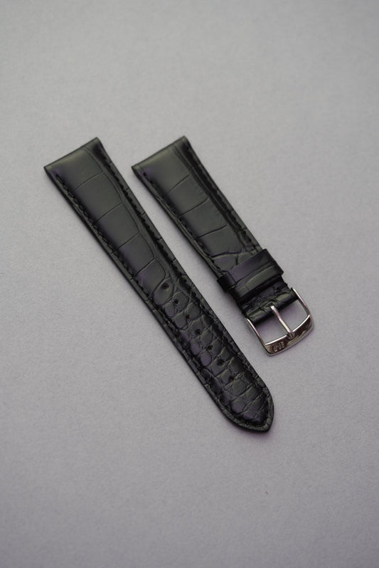 Black alligator embossed leather watch strap laid flat with polished stainless buckle