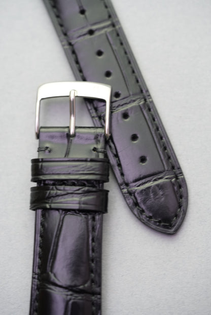 Close-up of black embossed alligator leather Apple Watch strap with stainless steel buckle.