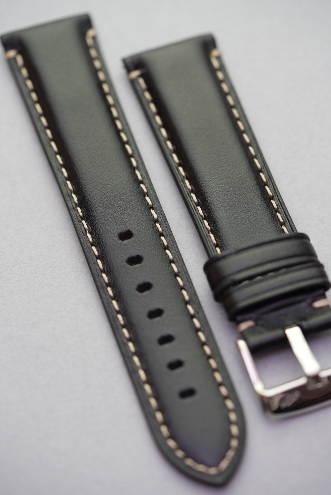 Angled view of black leather watch strap with cream contrast stitching