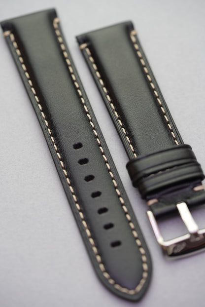Angled view of black leather watch strap with cream contrast stitching