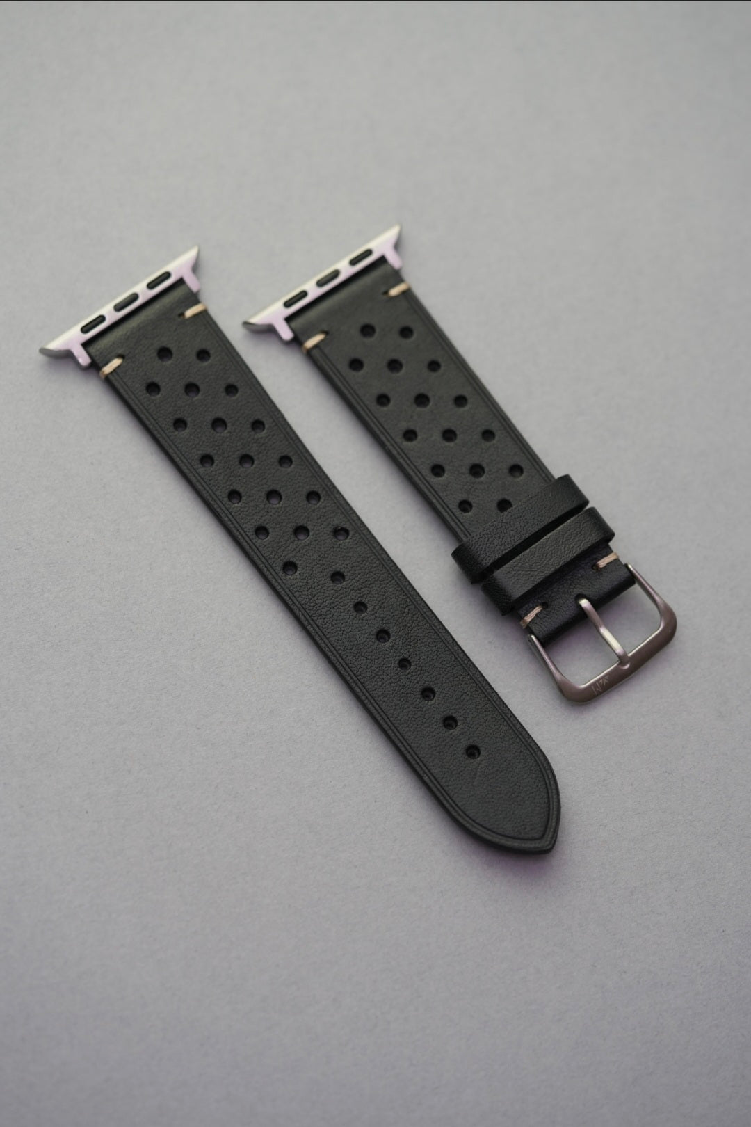 Perforated black leather strap with adapters for Apple Watch – flat lay view