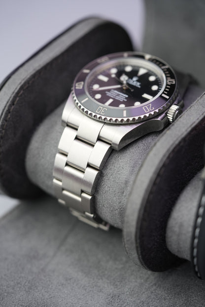 Close-up of Rolex Submariner on grey suede cushion inside the open black watch roll.