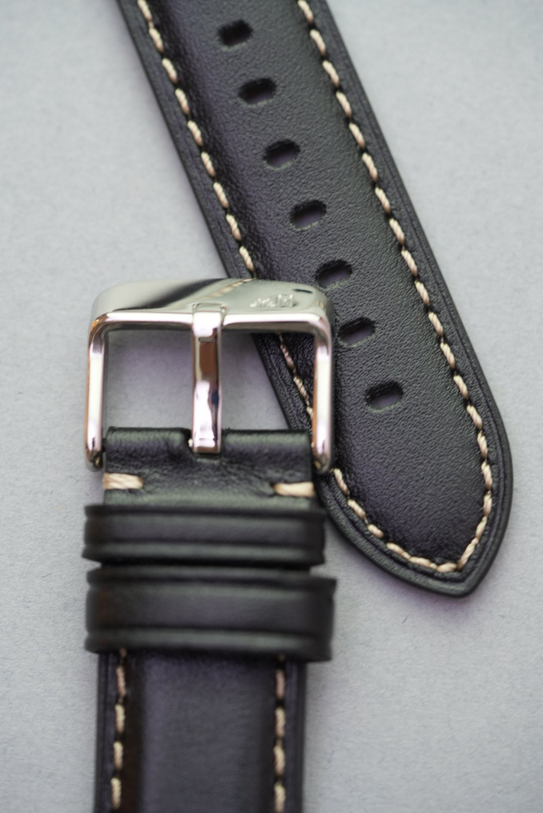 Stainless steel buckle and strap tip on black watch strap with cream stitching