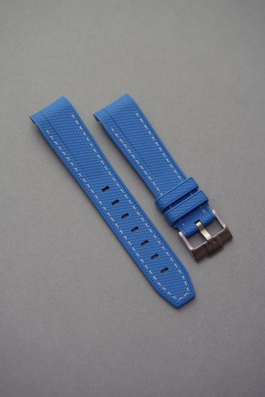 Bright blue rubber sailcloth-texture strap with white stitching, curved fit and brushed buckle for MoonSwatch watches.
