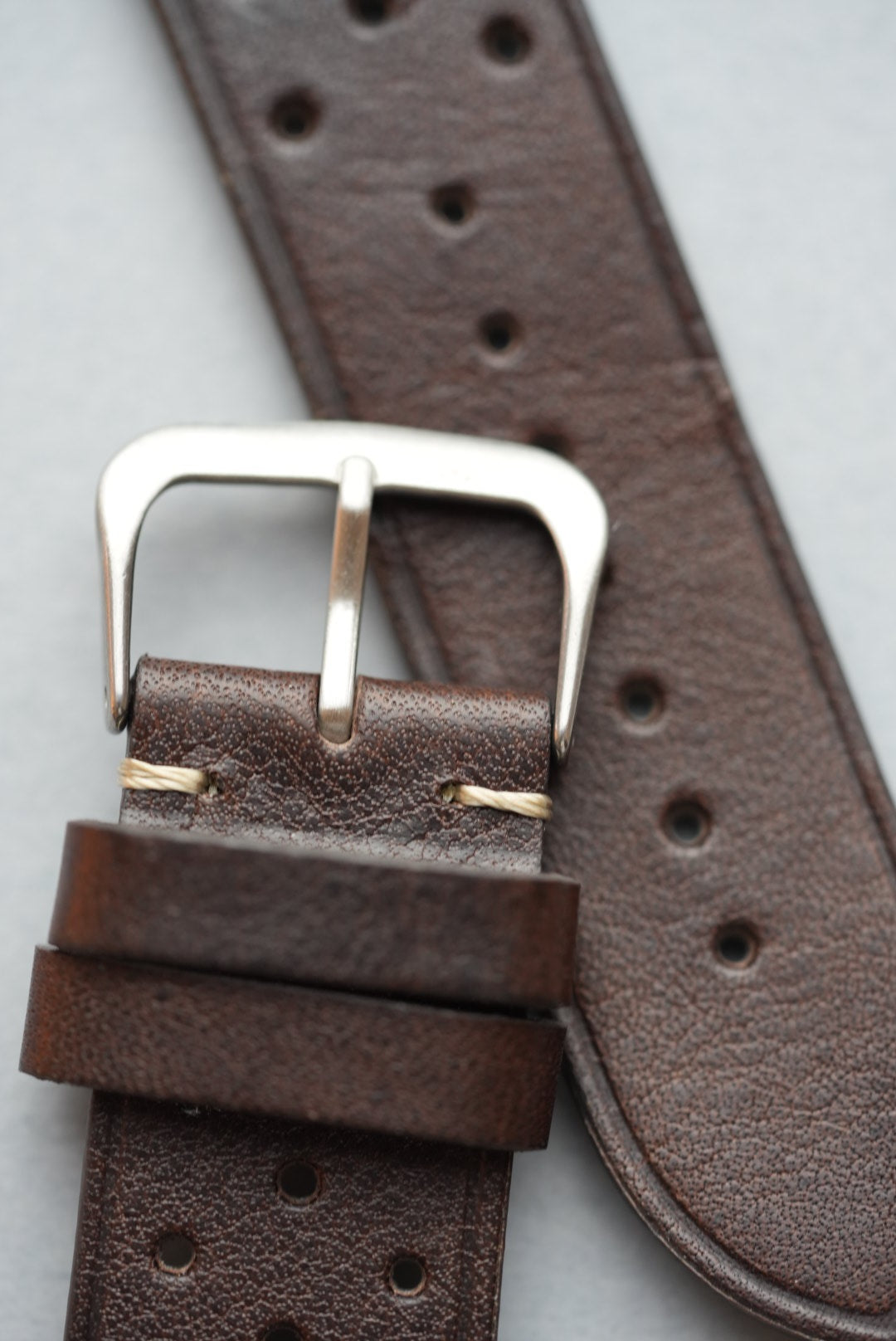 Angled close-up of brushed buckle and keeper loops on brown perforated strap