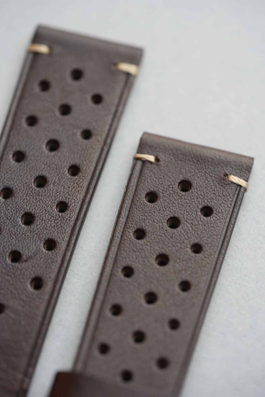 Angled close-up of brushed buckle and keeper loops on brown perforated strap